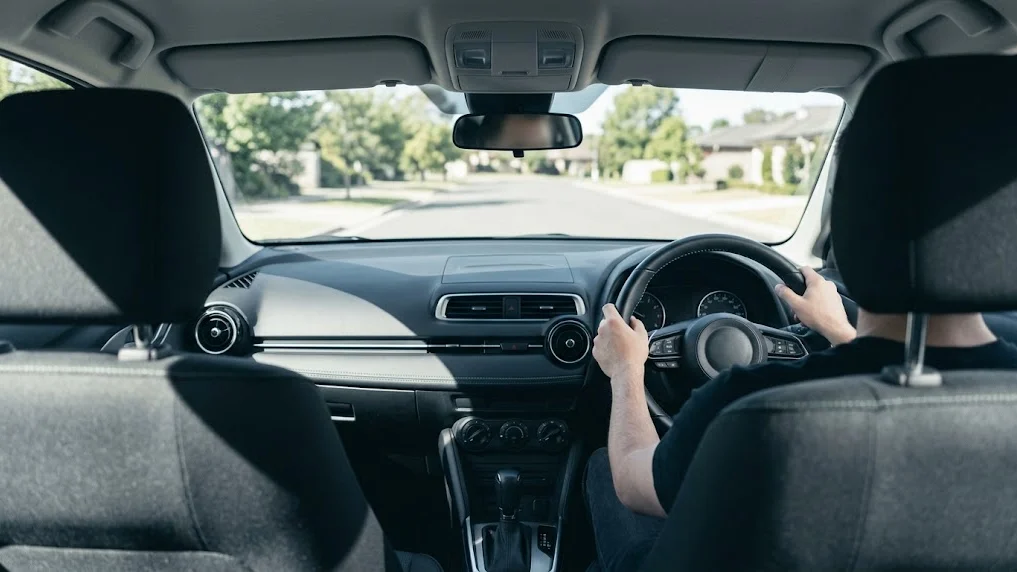 A customer driving a dealership courtesy vehicle through a residential street, the loan doubling as an extended test drive