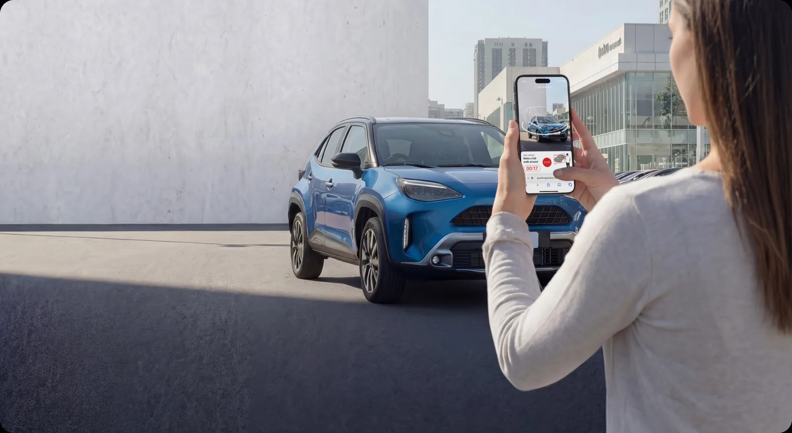 A person completing a guided walkaround of a blue compact SUV on their own phone, with the Self Inspection capture prompt on screen.